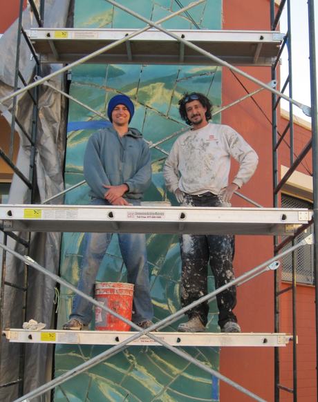 Dakota Warren painting a mural on scaffolding